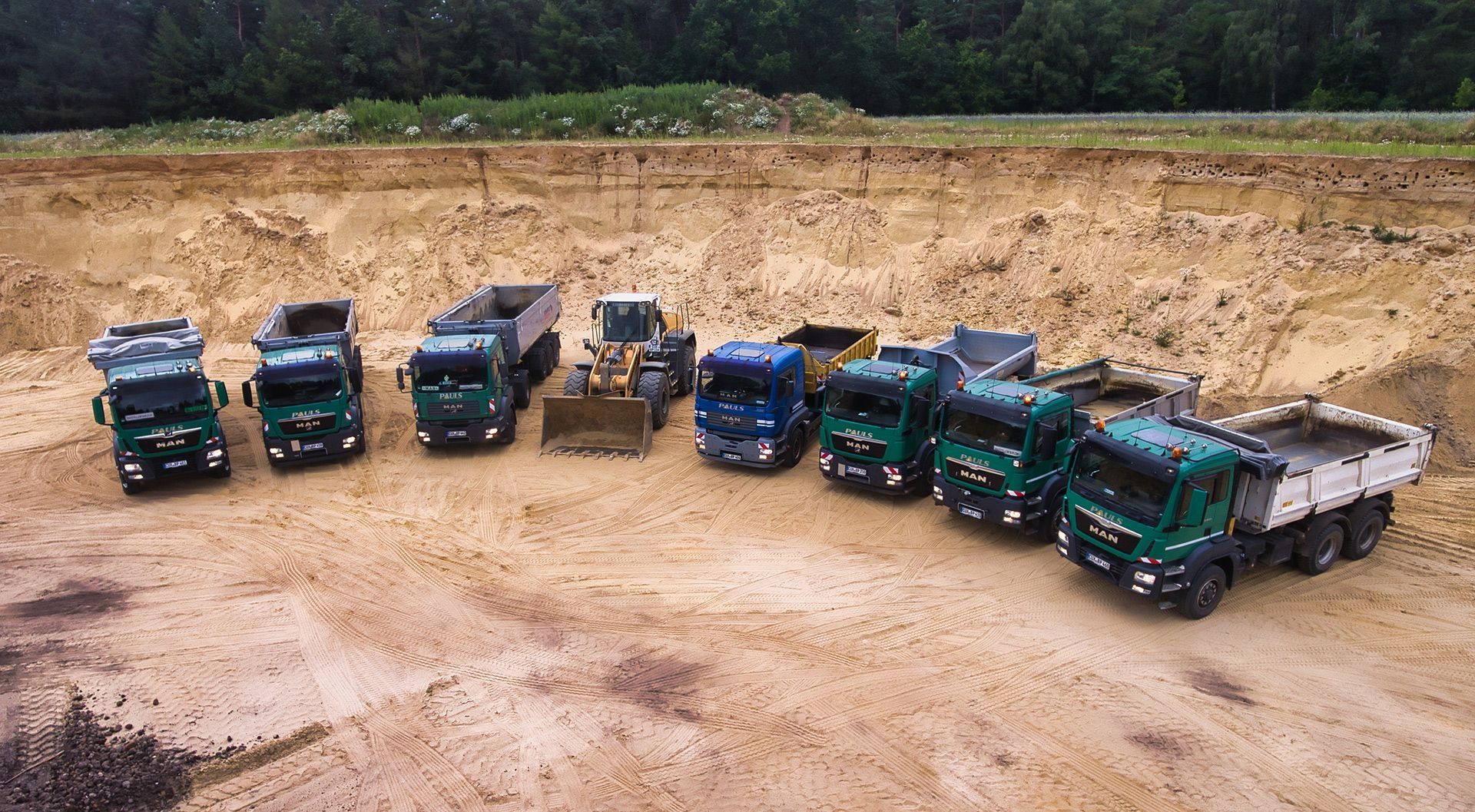 Eine Flotte von Baustellen-Lkw auf einer Baustelle im Sand.